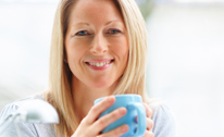 Woman smiling, holding a blue mug.